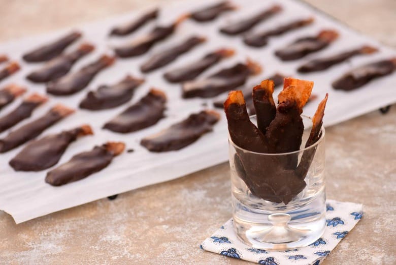 A photo of Chocolate Covered Bacon in a serving glass with a tray in the background
