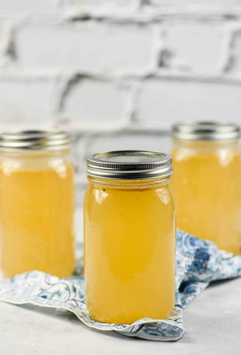 15 Health Benefits of Bone Broth - 3 jars of bone broth shown with a blue print napkin