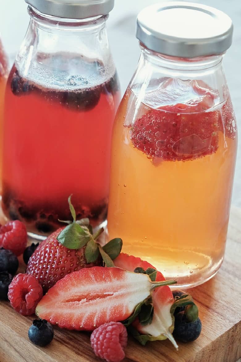 Flavored Kombucha shown in jars with fruit on a cutting board.