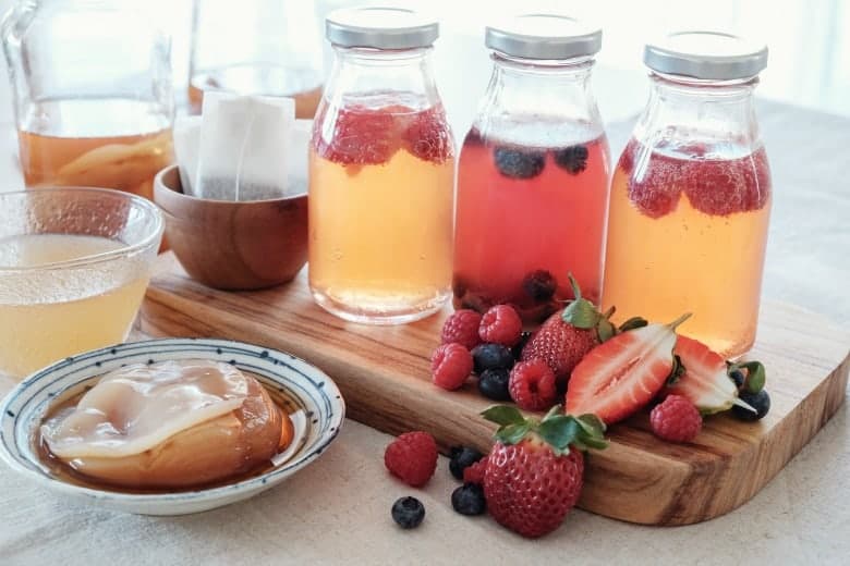 Flavored Kombucha shown in jars with fruit and scoby around.