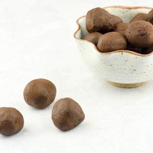 Three easy chocolate truffles recipe sitting on a white surface with a bowl in the background