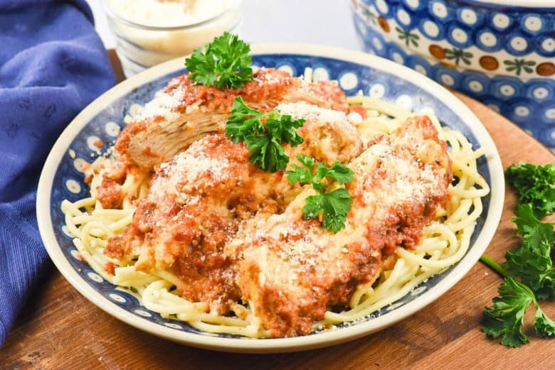 A close up of Crock Pot Chicken Parmesan on a white and blue plate garnished parsley