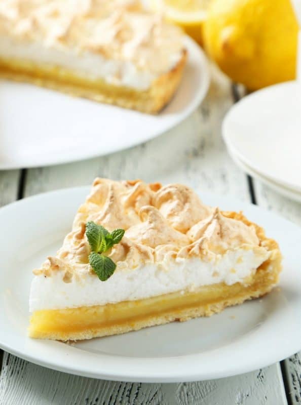 A slice of pie made from Grandma's Lemon Meringue Pie Recipe shown on a white plate with the pie in the background