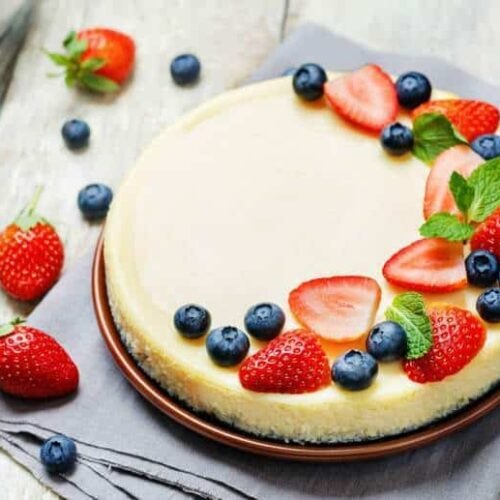 An overhead shot of Sour Cream Cheesecake topped with berries on a wooden surface