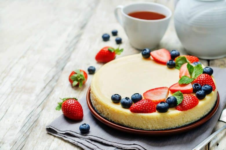 A side shot of Sour Cream Cheesecake topped with strawberries and blueberries