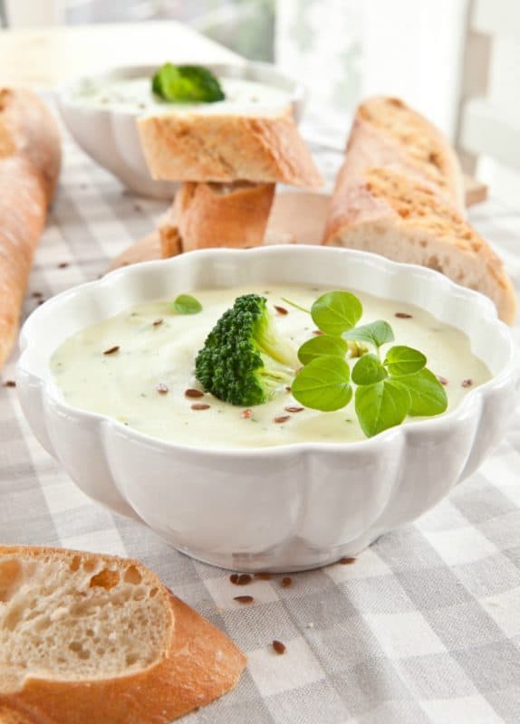 A photo of the best broccoli soup in a white bowl garnished with greens