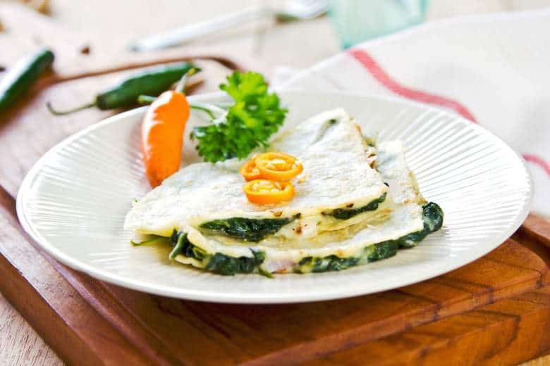 A photo of Easy Spinach Quesadillas on a white plate with slices of chili