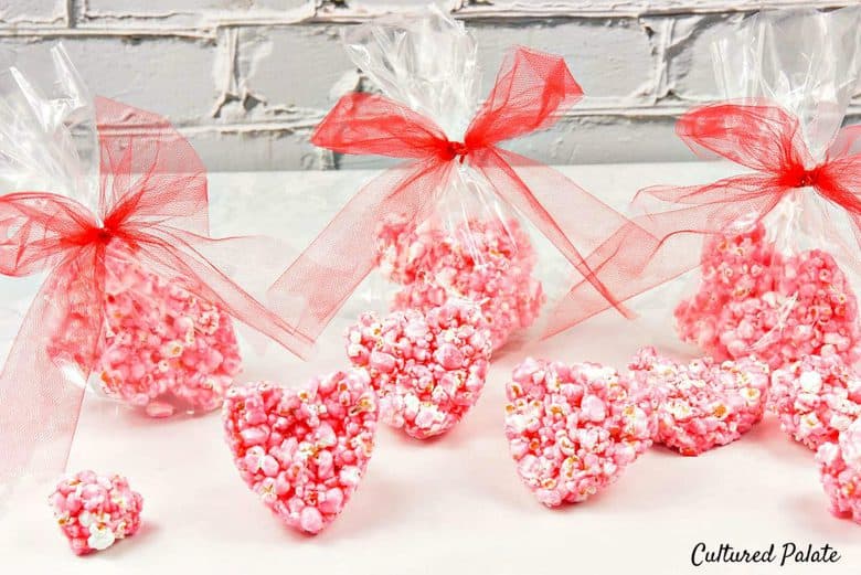 Heart shaped popcorn balls in red wrappers on a white surface