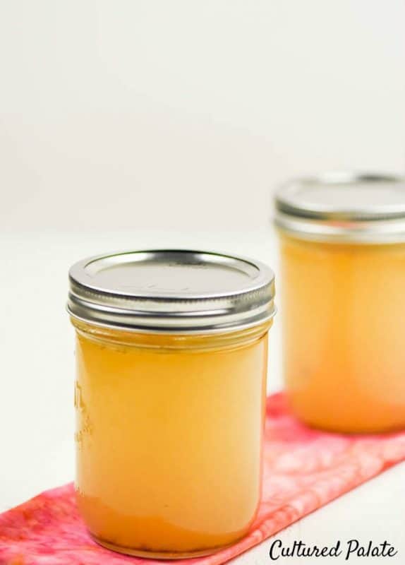 Vertical image showing a close-up jar of chicken broth - how to make chicken broth