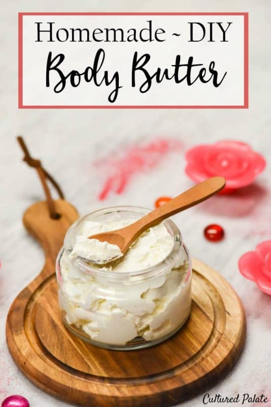 Whipped Body butter recipe made and put in a glass jar with wooden spoon, candles and glass beads around it