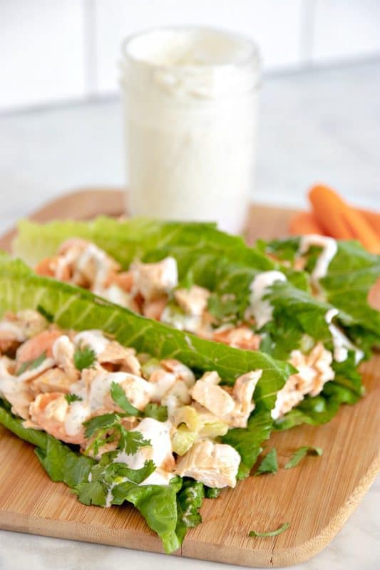 Vertical image showing Buffalo Chicken Lettuce Wraps on a cutting board with ranch dressing and carrots in the background