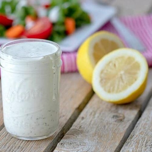 A jar of Homemade Ranch Dressing with lemons and veggies in the background