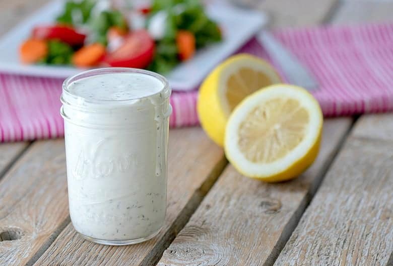 A jar of Homemade Ranch Dressing with lemons and veggies in the background