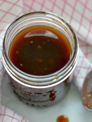 Homemade Teriyaki Sauce in a jar with spoon in background and checkered towel