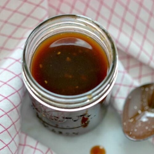 Homemade Teriyaki Sauce in a jar with spoon in background and checkered towel