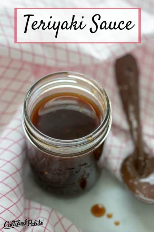 Titled vertical image of Homemade Teriyaki Sauce in a jar with spoon in background and checkered towel