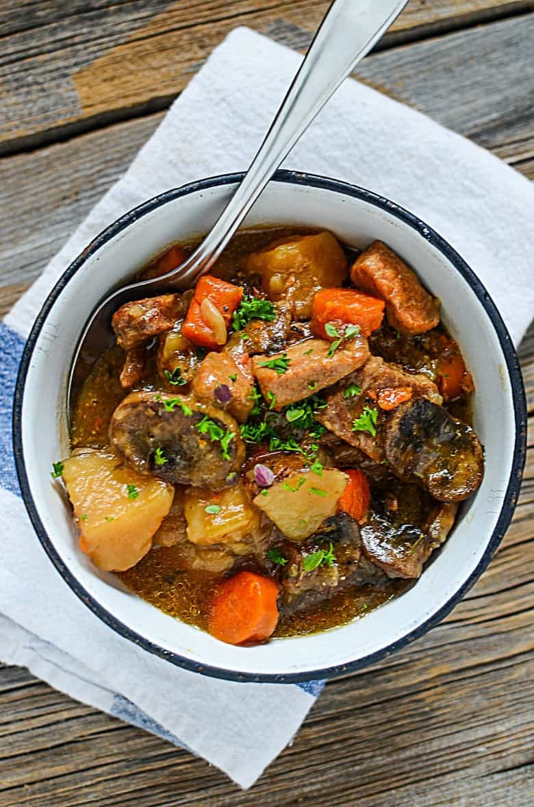 vertical photo of a white bowl of pork stew made in the instant pot on a wooden table