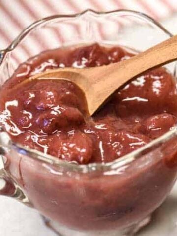 A glass dish shown withInstant Pot Strawberry Jam Recipe in it with wooden spoon.