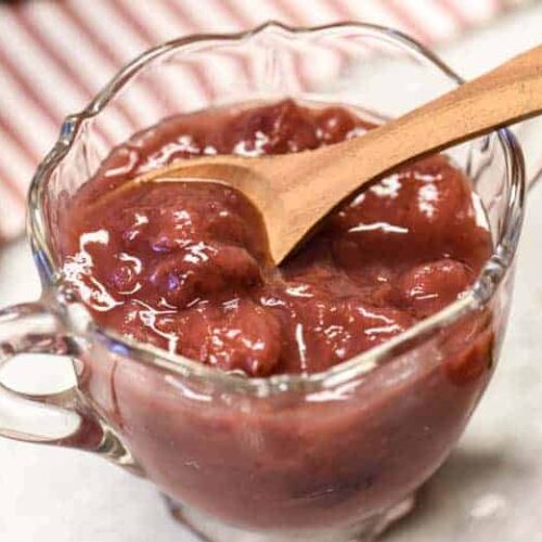 A glass dish shown withInstant Pot Strawberry Jam Recipe in it with wooden spoon.