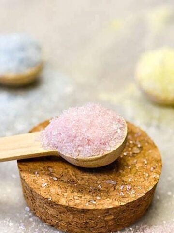 Closeup of homemade bath salts on a wooden spoon in pink, blue and yellow.