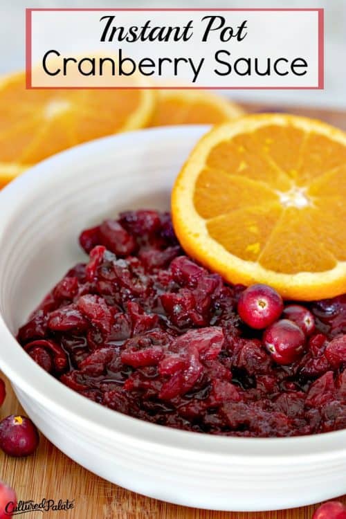 Titled vertical image of cranberry sauce in a white bowl with an orange slice on top.