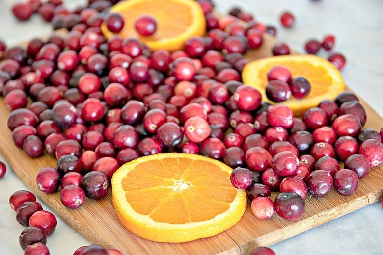 Ingredients for Cranberry Sauce recipe shown on wooden cutting board - cranberries and orange slices