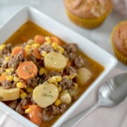 Instant Pot Beef Stew shown in a white bowl with muffins in the background.