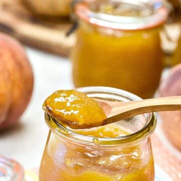 Instant Pot Peach Jam shown in a glass jar on a wooden spoon.