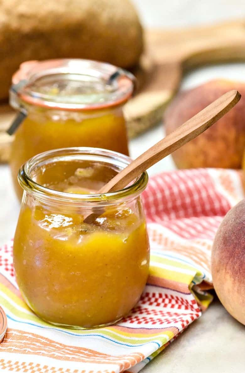 Vertical image of Instant Pot Peach Jam shown on a wooden spoon propped on a glass jar.