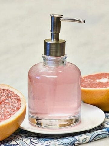 Homemade Body wash shown pink in a glass dispenser with two halves of grapefruit to either side