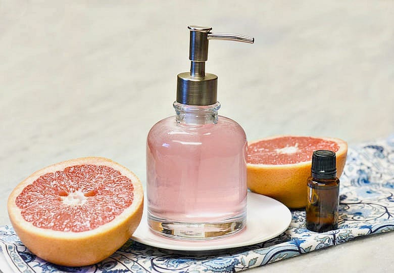 Homemade Body wash shown pink in a glass dispenser with two halves of grapefruit to either side