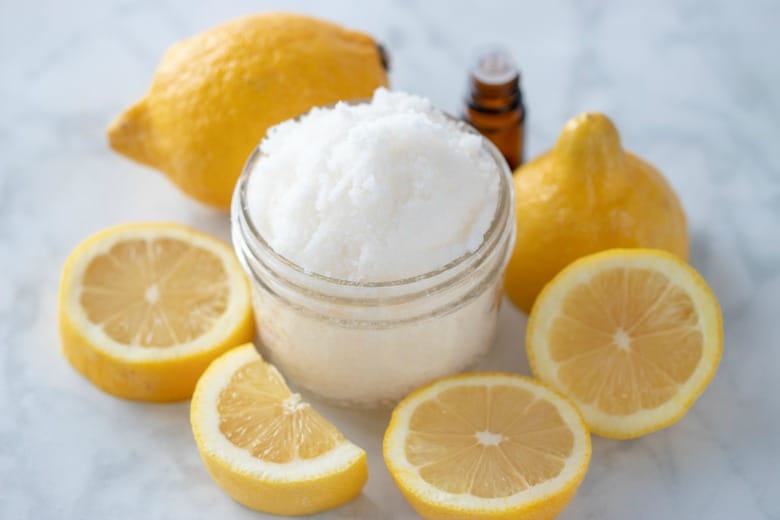 Horizontal image of Energizing Body Scrub with lemons around the glass jar.