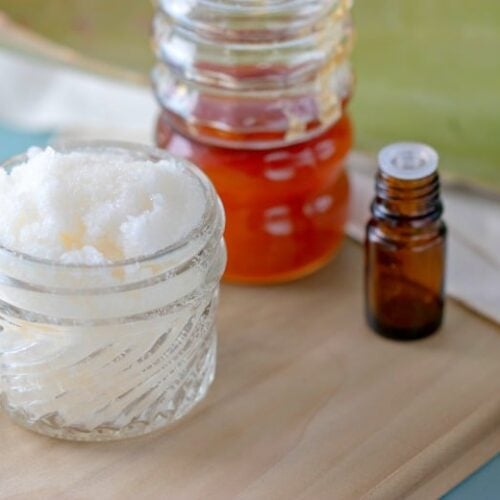 Body Scrub without Oil shown in glass jar with aloe, essential oil and honey in background on wooden board.