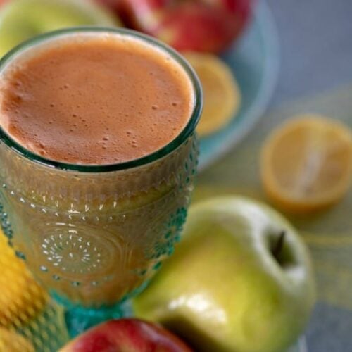 Carrot Celery Juice shown in glass with fruit around it.