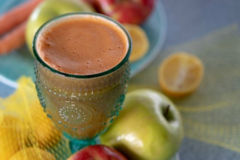 Carrot Celery Juice shown in glass with fruit around it.