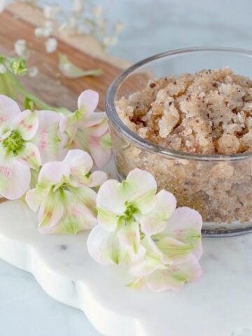 Homemade Sugar Exfoliating Scrub shown on marble cutting board with flowers to the side.