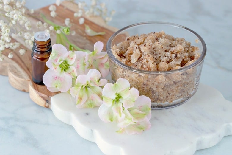 Homemade Sugar Exfoliating Scrub shown on marble cutting board with flowers to the side.