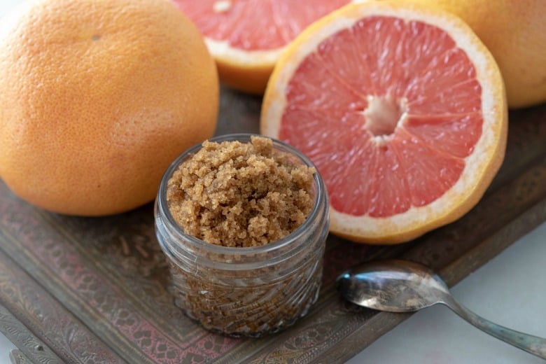 Moisturizing Sugar Scrub shown in glass jar with grapefruit around on tile.