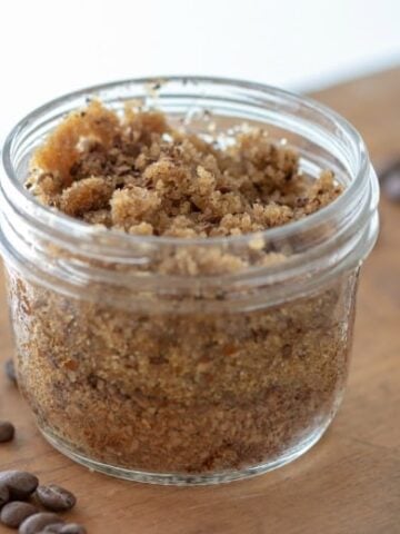 Peppermint Coffee Scrub shown in glass jar with coffee beans and essential oil around it.