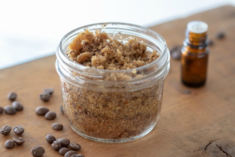 Peppermint Coffee Scrub shown in glass jar with coffee beans and essential oil around it.