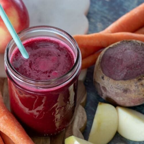 Red Carrot Juice shown with beets, carrots and apples around the jar.