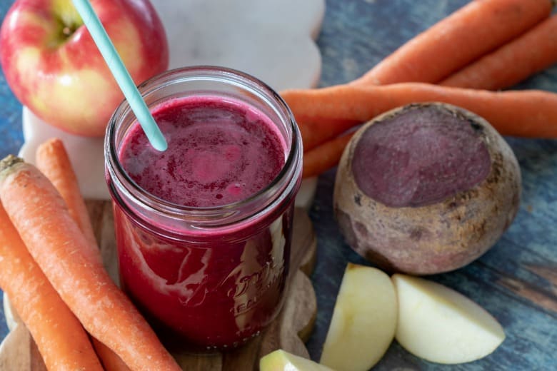 Red Carrot Juice shown with beets, carrots and apples around the jar.