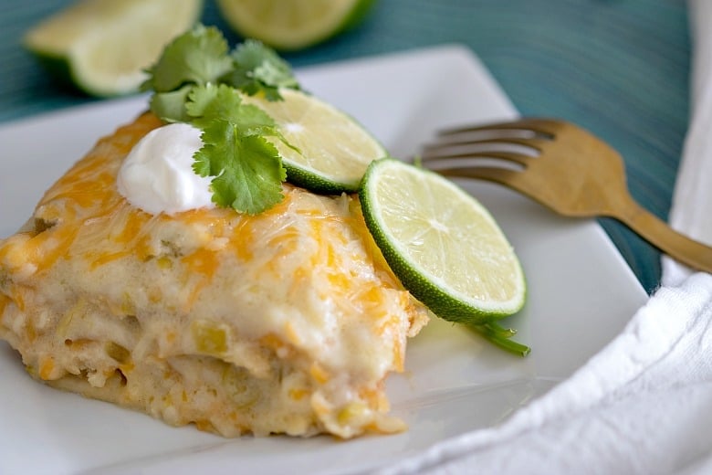 A piece of CrockpotÂ White Chicken Enchilada Casserole on a white plate with fork to the side.
