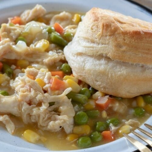 Crock Pot Chicken Pot Pie shown in horizontal image in white bowl with biscuit to side.