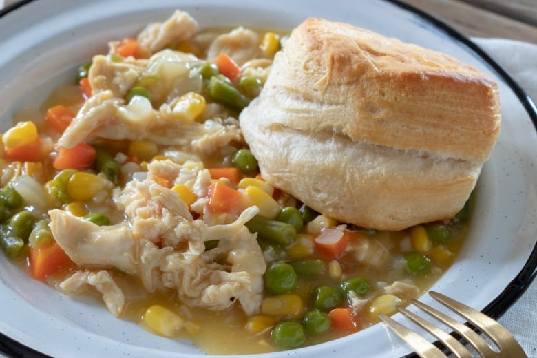Crockpot Chicken Pot Pie shown in horizontal image in white bowl with biscuit to side.