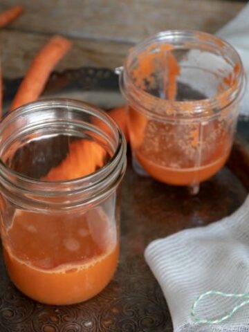 Carrot juice in jars with carrot around on tray from "How to Make Pure Carrot Juice