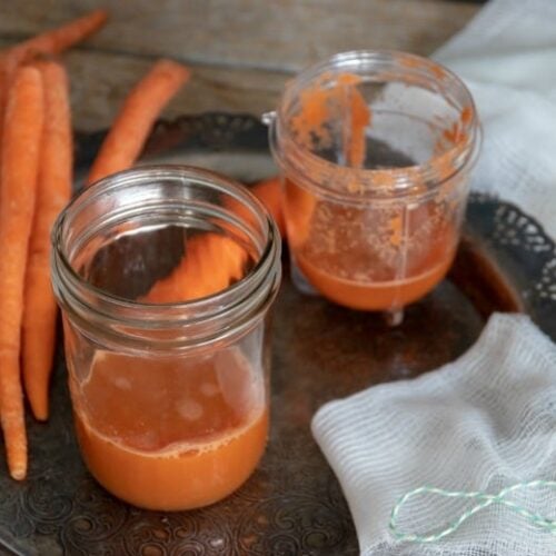 Carrot juice in jars with carrot around on tray from "How to Make Pure Carrot Juice