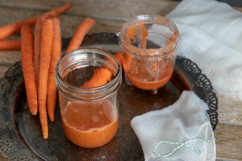 Carrot juice in jars with carrot around on tray from "How to Make Pure Carrot Juice