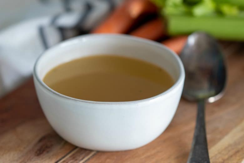 Crockpot Bone Broth shown on wooden table in a white bowl.