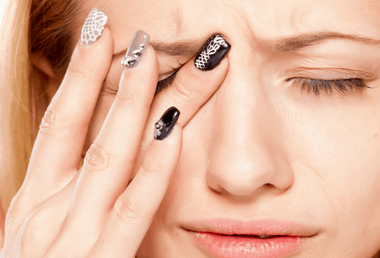 Horizontal image of a woman with fingers to her eye because of eye pain.
